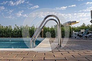 Blue swimming pool with beach lounger with parasol, sun deck on sea view for summer vacation