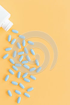 Blue tablets pills falling out of container on yellow background