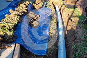 Blue tarp, black mixing tub container with dirt, underground PVC pipe buried in trench installation, rainwater drainage system