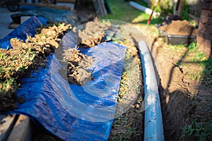 Blue tarp, black mixing tub container with dirt, underground PVC pipe buried in trench installation, rainwater drainage system