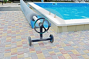 Blue tarpaulin pool cover and mechanical reel. Bubble awning film for covering the pool. Pool with blue water.