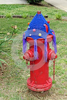 Blue tassel and pom-pom hat yarn bomb on city red fire extinguisher