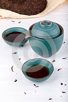 Blue teapot and two small cups full of puer tea on white table