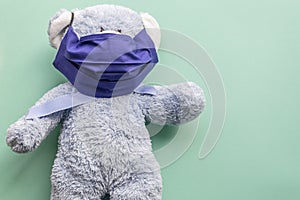 Blue teddy bear in a dark blue reusable mask on a mint plain background. Place for text on the right. Medecine