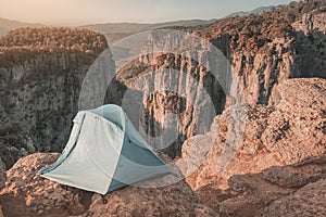 blue tent is set on top of a cliff above a deep canyon with stunning mountain views. Concept of extreme rock climbing and