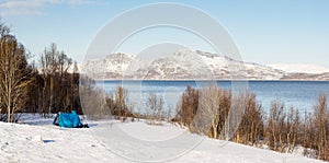 Blue tent on a snowy field in the polar area with a view on a fjord and mountains covered in snow near Tromso Norway