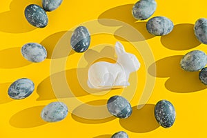 Blue textured colored Easter eggs and white plactic bunny on a bright yellow holiday background backdrop. Spring holiday