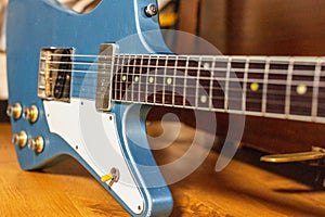 A blue Theta guitar sits on a wooden floor next to a piano
