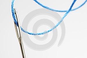 Blue thread going through needle eye close-up