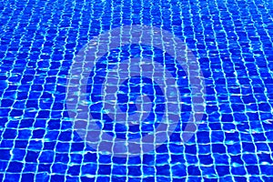 The blue tiles floor under the clear water in the swimming pool background, Swimming pool surface with floor mosaic tiles in blue