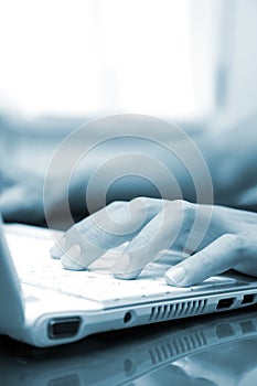 Blue toned image of a man typing on his laptop