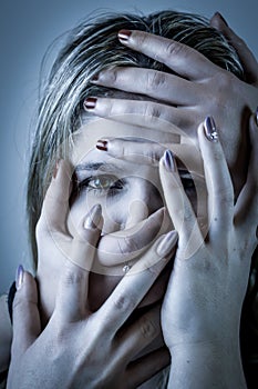 Blue toned portrait of a young woman with her face covered with hands, concept for showing the anxieties and fears of women