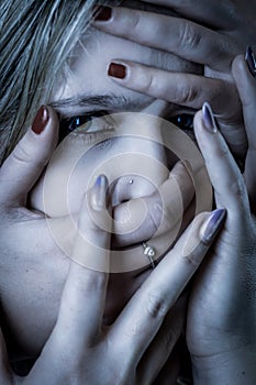 Blue toned portrait of a young woman with her face covered with hands, concept for showing the anxieties and fears of women