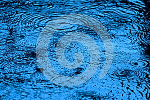 Blue toned water surface ripples and splashes in the falling rain