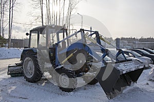 Blue tractor with a blade for snow removal in winter and a spinning brush for street cleaning