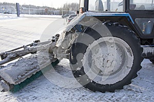 Blue tractor with a blade for snow removal in winter and a spinning brush for street cleaning