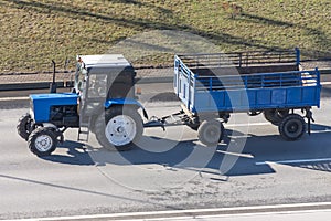 A blue tractor with an empty freight trailer rides in the city on a highway