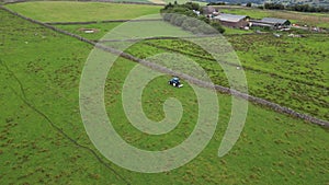 Blue tractor farming on a green field in North Yorkshire England drone aerial videography