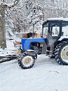 a blue tractor with large wheels in a snowy forest.