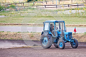 A blue tractor levels the dirt road, kicking up a cloud of dust behind. copy space