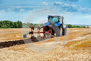 Blue tractor pulls plow, arable land, field preparation