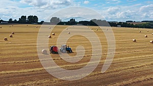 A blue tractor with a red baler collects straw into bales.