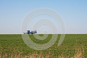 Blue tractor sprinkles wheat, blue harvester sprinkles wheat, blue tractor sprinkles field from pests, tractor sprinkles green fie