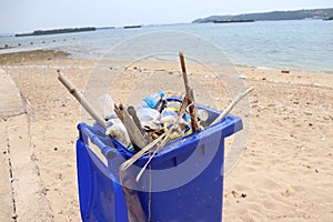 Trash bin beside the sandy beach and full of plastic waste