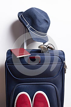 blue travel suitcase with passport, hat, shoes, glasses