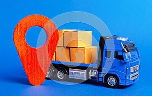 A blue truck loaded with boxes and a red pointer location. Services transportation of goods, products, logistics