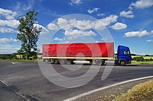 Blue truck with red sail passing a crossroads in the countryside