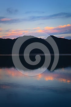 Blue twilight sky and dark mountains reflected on the calm waters of a lake. Calm, peaceful scene.