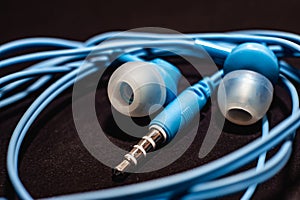 Blue twisted wired headphones on a monochromatic black surface, close-up. Headset for a mobile phone. Music.