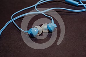 Blue twisted wired headphones on a monochromatic black surface, close-up. Headset for a mobile phone. Music