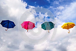 Blue Umbrella, Red Umbrella, Green Umbrella and Yellow Umbrella floating in the Air under Blue Sky and Clouds