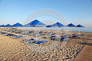 Blue umbrellas and chaise longue on empty sandy beach, Greece