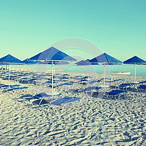 Blue umbrellas and chaise longue on empty sandy beach, Greece