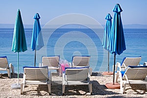 Blue umbrellas and chaise for relax on sea coast. Happy summer vacations and travel concept. Paid service on beaches