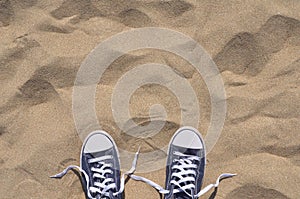 Blue unlaced sneakers on beach, top view