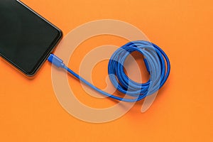 Blue USB cable and smartphone on an orange background. Flat lay