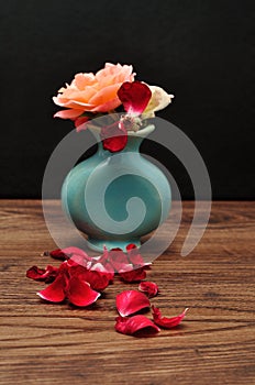 A blue vase with rose where one has lost its petals