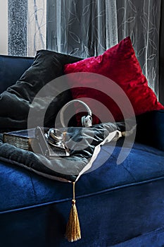 A blue velvet sofa with colorful cushions, a vintage photo camera, a cushion with tassels and white curtains