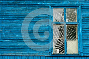 The blue wall of an old dilapidated wooden house and a glass window. The concept of living in a village in an ecologically clean