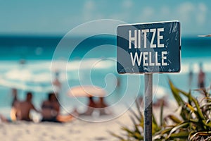 Blue warning sign with German text \'Hitzewelle\' (Heat wave) in front of blurry sunny beach with people