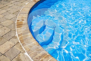 Blue water in-ground pool with steps into the water from a brick platform indoors or outdoors