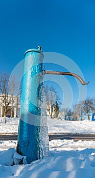 Blue water pump covered with ice, the water froze on the drinking column, water well ice