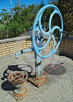 Blue water well pump, with wheel, on summer sun