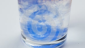 Blue watercolor paint drops dissolve on water in glass