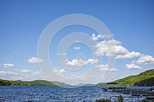 The blue waters of Otsego Lake in Cooperstown, New York, on a sunny summer day with cumulus clouds in the sky, photographed near a
