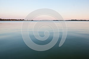 Blue waters of the Palic Lake, in Subotica, Serbia, with a green lawn in the background, during a summer sunset